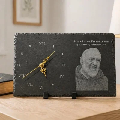 Engraved Padre Pio slate clock with Roman numerals and gold hands displayed on wooden table